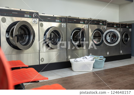 Row of washing machines in public laundromat and basket with dirty clothing on the floor Row of washing machines in public laundromat and basket with dirty clothing on the floor 124648157
