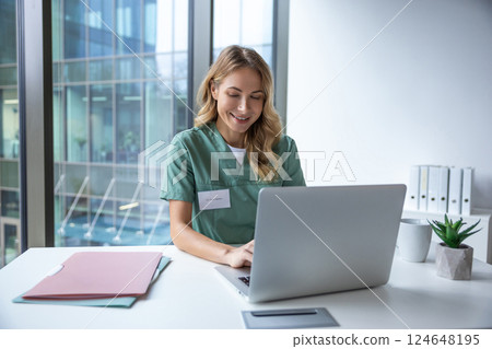 Female doctor in uniform sitting in hospital office working on laptop Female doctor in uniform sitting in hospital office working on laptop 124648195