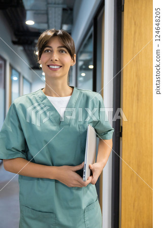Professional physician in uniform in clinic hallway carrying computer Professional physician in uniform in clinic hallway carrying computer 124648205