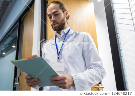 Male doctor standing in hospital corridor holding case history and medical documents 124648217