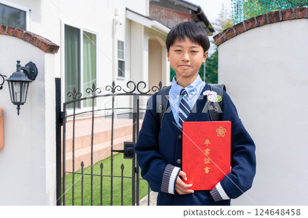 Elementary school boy holding a diploma in front of his home 124648458