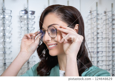 Pretty young dark-haired woman trying on new glasses 124648629