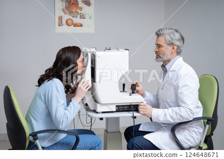 Gray haired man doctor examining woman patient eyes with professional technology 124648671