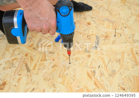 Man using blue cordless drill on wooden OSB board. Man using blue cordless drill on wooden OSB board. 124649395