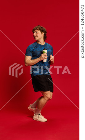 Dynamic photo of young male athlete smiling while holding battle against red studio background, enjoying post-workout break. 124650473