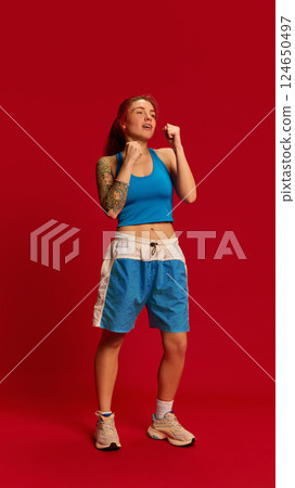Dynamic photo of young female athlete parrying punches during martial arts training. Girl stands in basic position against red studio background. 124650497