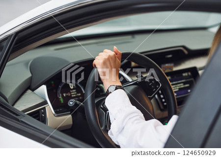 Sitting and driving. Young woman in white clothes is with her electric car at daytime 124650929