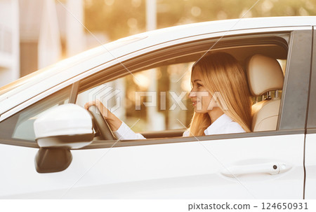 Sitting and driving. Young woman in white clothes is with her electric car at daytime Sitting and driving. Young woman in white clothes is with her electric car at daytime 124650931