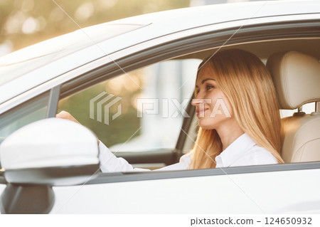 Sitting and driving. Young woman in white clothes is with her electric car at daytime 124650932