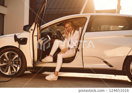 Illuminated by sunlight. Young woman in white clothes is with her electric car at daytime 124651016