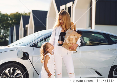 With shopping bags. Young woman with her little daughter is with their electric car outdoors 124651112