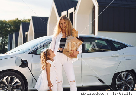 With shopping bags. Young woman with her little daughter is with their electric car outdoors 124651113