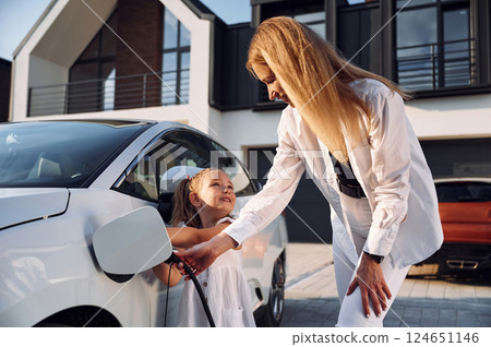 Young woman with her little daughter is with their electric car outdoors Young woman with her little daughter is with their electric car outdoors 124651146