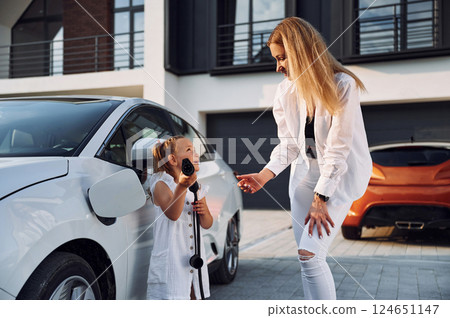 Young woman with her little daughter is with their electric car outdoors Young woman with her little daughter is with their electric car outdoors 124651147