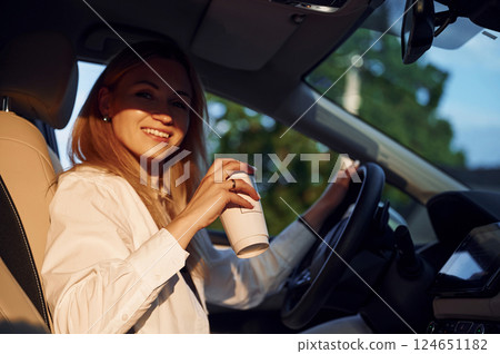 With cup of drink. Young woman in white clothes is with her electric car at daytime 124651182