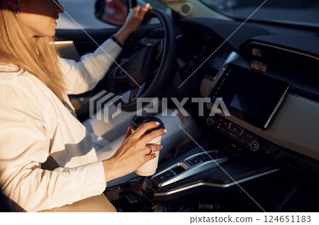 With cup of drink. Young woman in white clothes is with her electric car at daytime 124651183