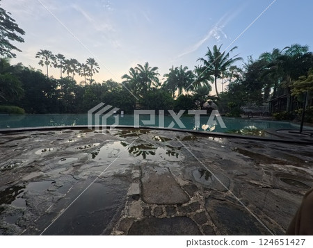 A serene pool reflects palm trees at dawn. Tranquil scene with a glimpse of a building and lush greenery. Peaceful and inviting. 124651427