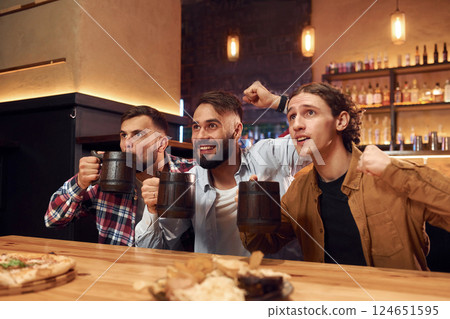 Soccer fans watching match. Three friends are in the bar drinking beer and having a good time Soccer fans watching match. Three friends are in the bar drinking beer and having a good time 124651595