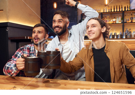 Soccer fans watching match. Three friends are in the bar drinking beer and having a good time Soccer fans watching match. Three friends are in the bar drinking beer and having a good time 124651596
