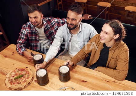 Top view. Sitting by the table. Three friends are in the bar drinking beer and having a good time Top view. Sitting by the table. Three friends are in the bar drinking beer and having a good time 124651598