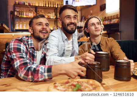 Front view. Soccer fans. Three friends are in the bar drinking beer and having a good time Front view. Soccer fans. Three friends are in the bar drinking beer and having a good time 124651610