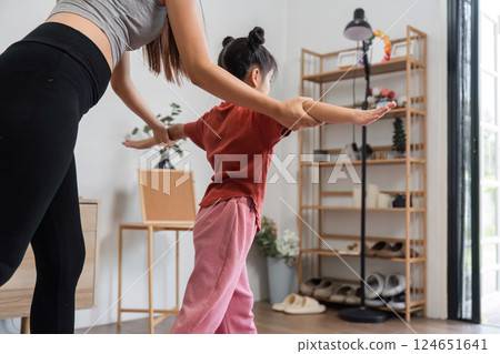 Balance and Fitness Fun. A mother guiding her daughter in maintaining balance during a home workout. 124651641