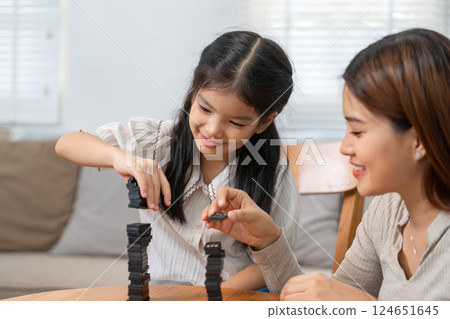 Family Bonding and Play. A mother and daughter joyfully stacking dominoes together at home. 124651645