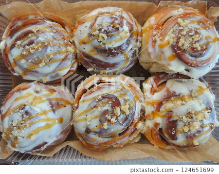 six homemade twisted buns with glaze and nut sprinkles lying on brown parchment paper, freshly baked cinnabons close-up with sweet white filling and nut crumbs six homemade twisted buns with glaze and nut sprinkles lying on brown parchment paper, freshly baked cinnabons close-up with sweet white filling and nut crumbs 124651699