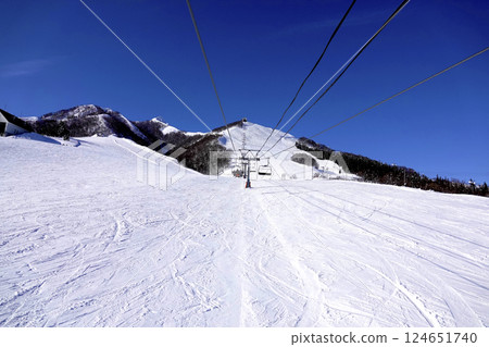 A ski resort on a clear day with a lift leading to the summit and a vast, pure white slope 124651740