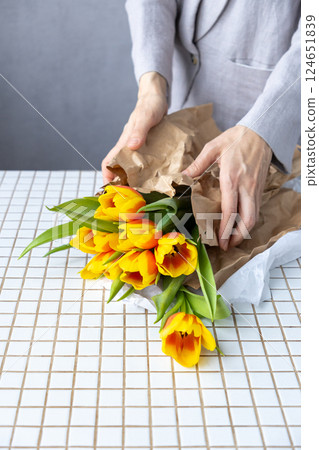female florist packs flowers in kraft paper, bouquet of yellow-red tulips. birthday mother's day. female florist packs flowers in kraft paper, bouquet of yellow-red tulips. birthday mother's day. 124651839