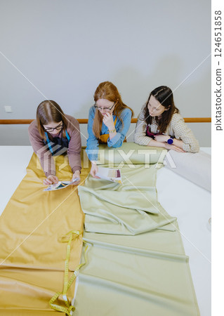 Top view of three women seamstresses, fashion designers standing at a table with a roll of fabric 124651858