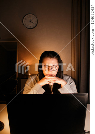 Woman working on computer late evening at home office. Concentrated female freelancer trying to solve business problems. Working and suffering from weariness. 124652434