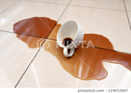Spilled coffee, coffe puddle stain on tiled floor, messy leak with fallen cup, brown drink spillage 124652607