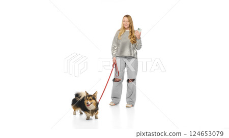 Purebred, funny and playful Corgi on leash looking away while woman smiles and holds phone against white background. Concept of pet walk Purebred, funny and playful Corgi on leash looking away while woman smiles and holds phone against white background. Concept of pet walk 124653079