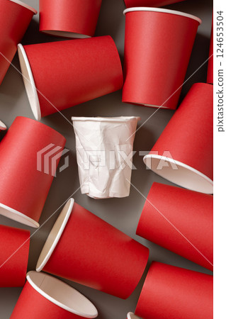 New red paper cups and crumpled used white one on a gray top view. Consumerism concept New red paper cups and crumpled used white one on a gray top view. Consumerism concept 124653504