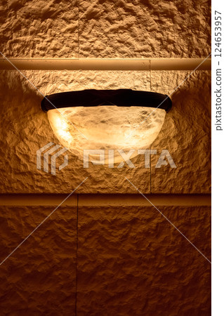 Warm-lit semi-spherical sconce on natural stone surface 124653957