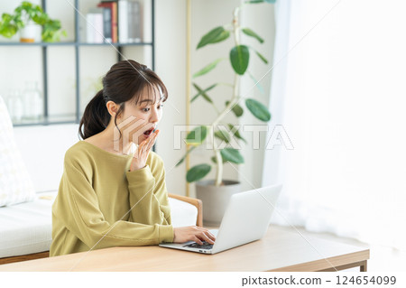 使用一台電腦在客廳裡的年輕女子 使用一台電腦在客廳裡的年輕女子 124654099