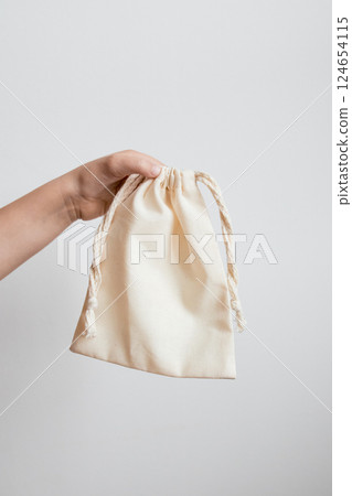 Hand holding eco friendly cotton drawstring bag against white background 124654115