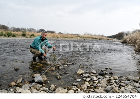 一位穿著防水褲的漁民用抄網捕捉河裡的昆蟲 124654704