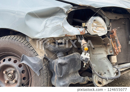 A close-up of a damaged car shows a crumpled fender, exposed headlight components, and bent metal after a collision 124655077
