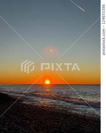 Sunset over pebble beach with ocean waves and sky contrails 124655386