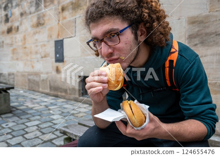 Nuremberg, Germany, August 1, 2023. A young Caucasian man enjoys a break eating sandwiches with typical Nuremberg sausage. Close up on the sandwich. Relax, lifestyle, local food. 124655476