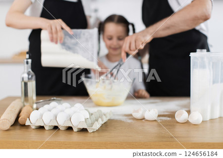 Caucasian family, including young girl and adults, whisking and mixing ingredients during cooking activity in a kitchen. Kitchen activity displaying collaboration, joy, and togetherness. Caucasian family, including young girl and adults, whisking and mixing ingredients during cooking activity in a kitchen. Kitchen activity displaying collaboration, joy, and togetherness. 124656184