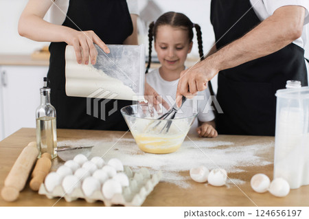 Caucasian man, woman, and girl baking together in kitchen mixing ingredients with whisk. Caucasian man, woman, and girl baking together in kitchen mixing ingredients with whisk. 124656197