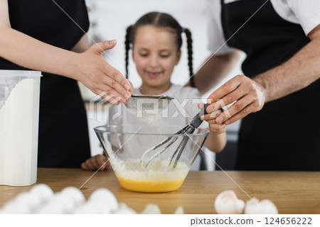 Caucasian family in kitchen cooking together. Parents and child prepare batter using whisk. 124656222
