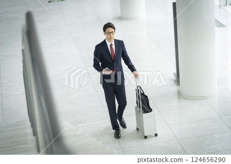 A businessman in his 40s walking with a smartphone and a suitcase 124656290