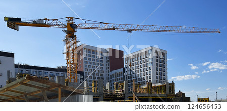 Construction crane towering over a residential building site under clear blue sky. Ongoing development with modern apartment buildings in the background and steel framework Construction crane towering over a residential building site under clear blue sky. Ongoing development with modern apartment buildings in the background and steel framework 124656453