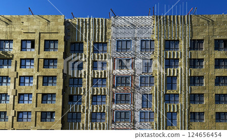 Multi-story building under renovation, showcasing exposed insulation layers and unfinished facade. The construction process is visible, steps in facade upgrade Multi-story building under renovation, showcasing exposed insulation layers and unfinished facade. The construction process is visible, steps in facade upgrade 124656454