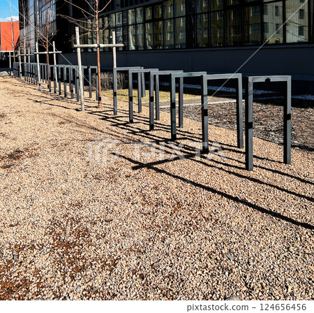 Empty metal bike racks lined up on gravel path outside a modern building, casting distinct shadows on the ground in quiet urban setting copy space Empty metal bike racks lined up on gravel path outside a modern building, casting distinct shadows on the ground in quiet urban setting copy space 124656456