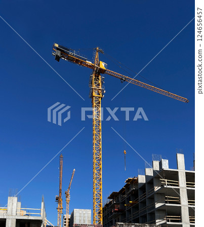 Tower cranes in action on a construction site. High-rise buildings under development showcase crane operations for lifting materials against blue sky , industrial scene Tower cranes in action on a construction site. High-rise buildings under development showcase crane operations for lifting materials against blue sky , industrial scene 124656457
